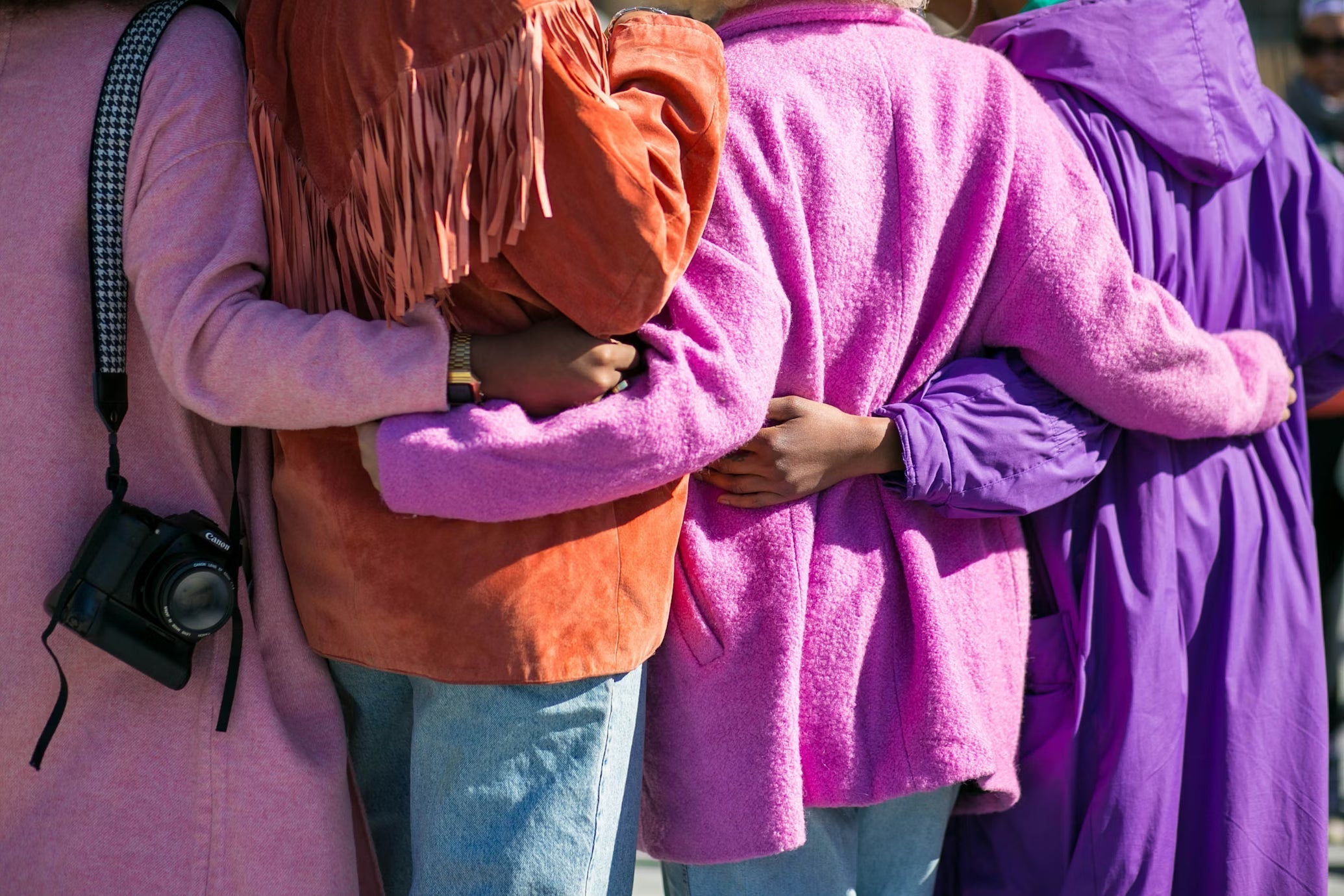 Women standing arm in arm in pink and purple tones celebrating International Women’s Day and female empowerment