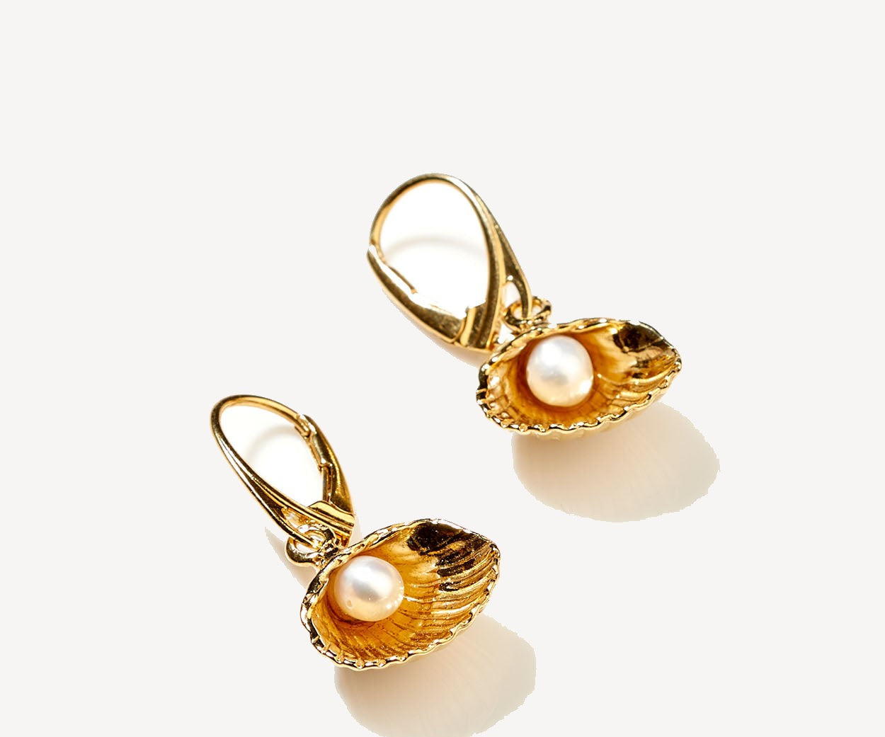 Gold earrings with pearl inside an oyster shell on a white background