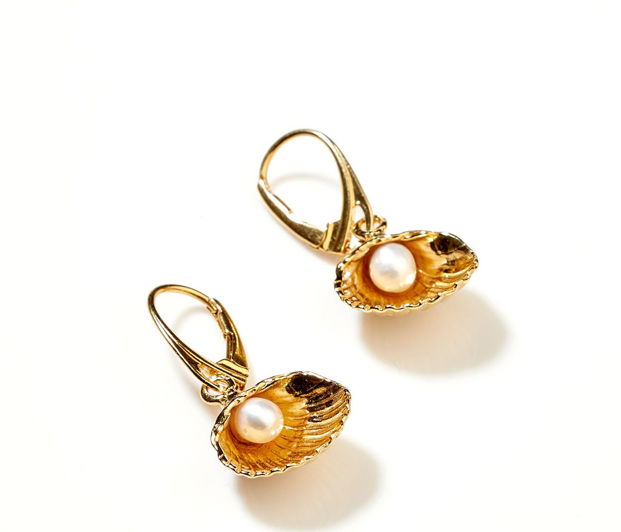 Gold earrings with pearl inside an oyster shell on a white background
