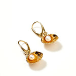Gold earrings with pearl inside an oyster shell on a white background