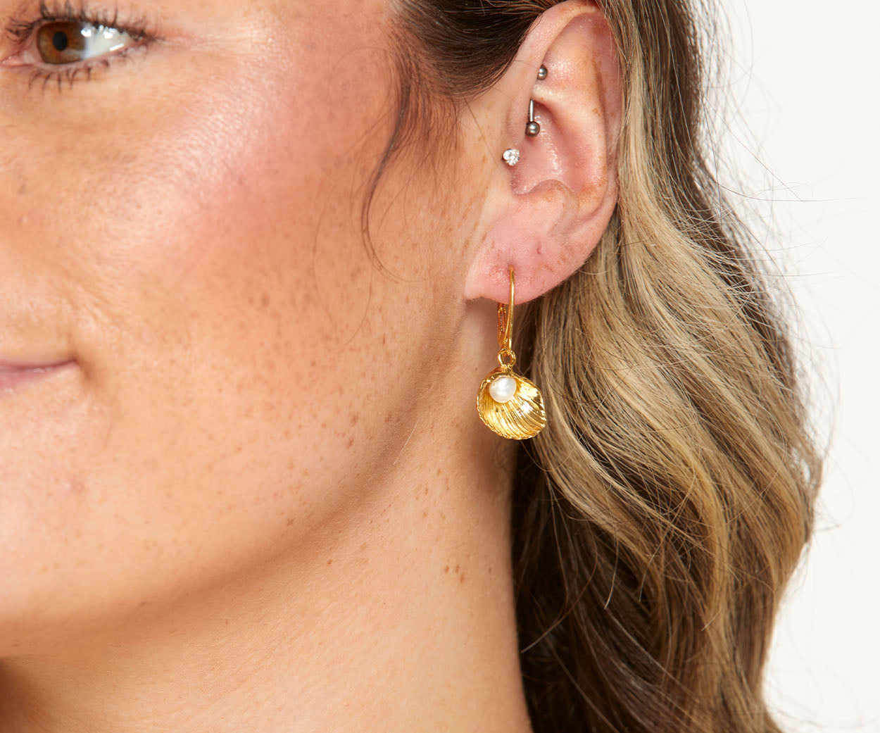 Close-up of a person wearing a gold earring with a pearl-like bead on a neutral background