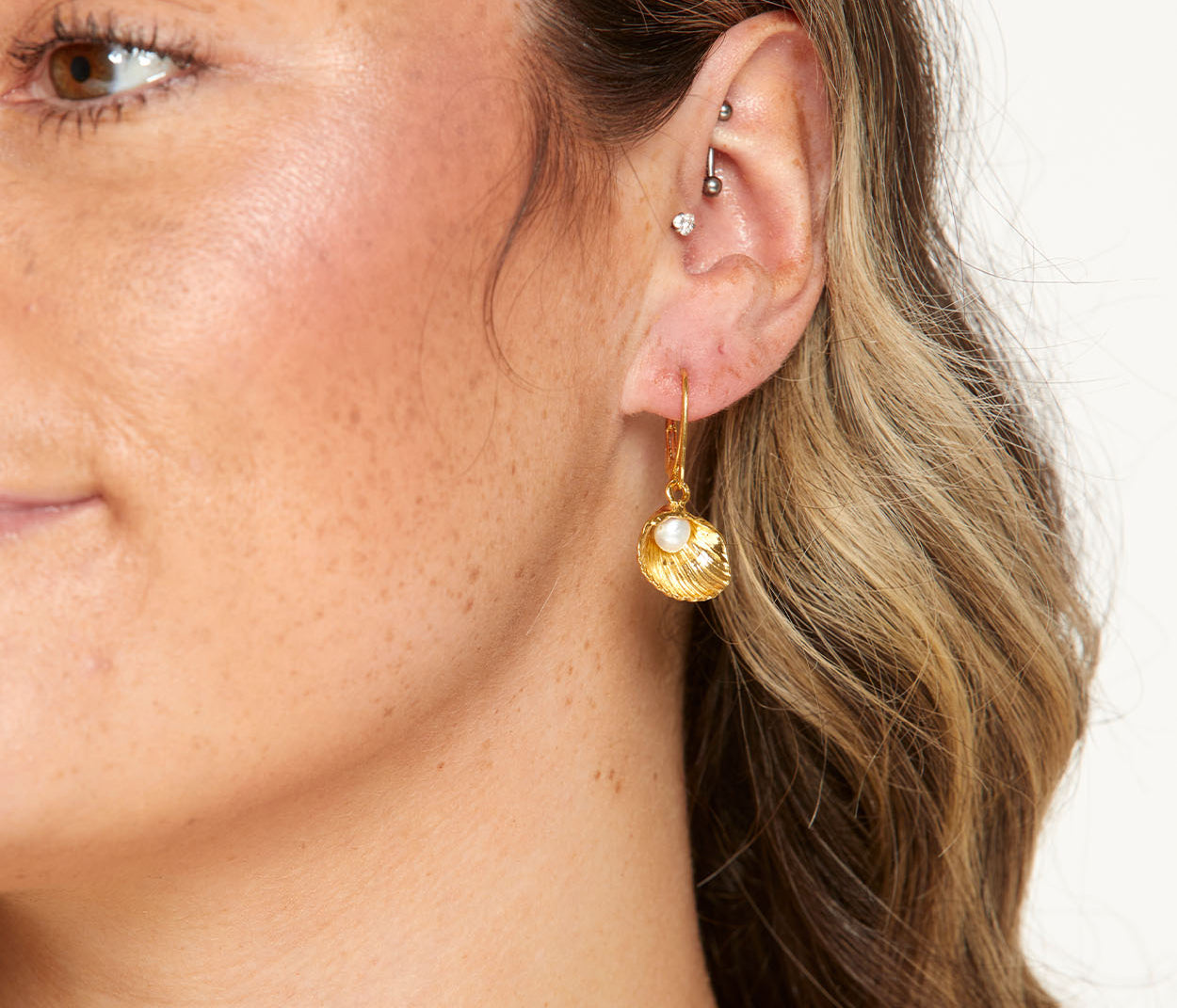Close-up of a person wearing a gold earring with a pearl-like bead on a neutral background