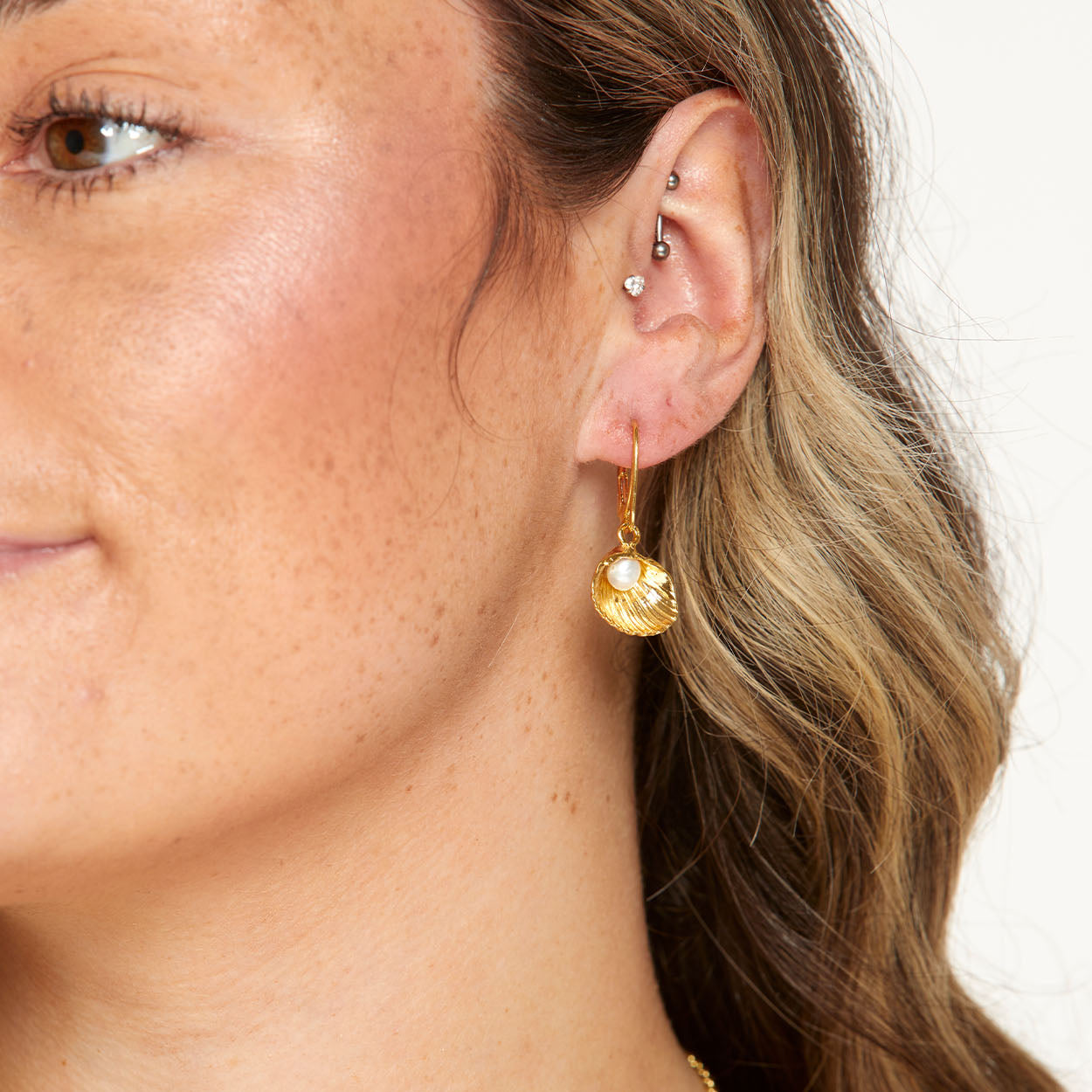 Close-up of a person wearing a gold earring with a pearl-like bead on a neutral background