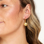 Close-up of a person wearing a gold earring with a pearl-like bead on a neutral background